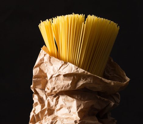 Bunch of spaghetti in craft paper bag on antique table. Dark background.